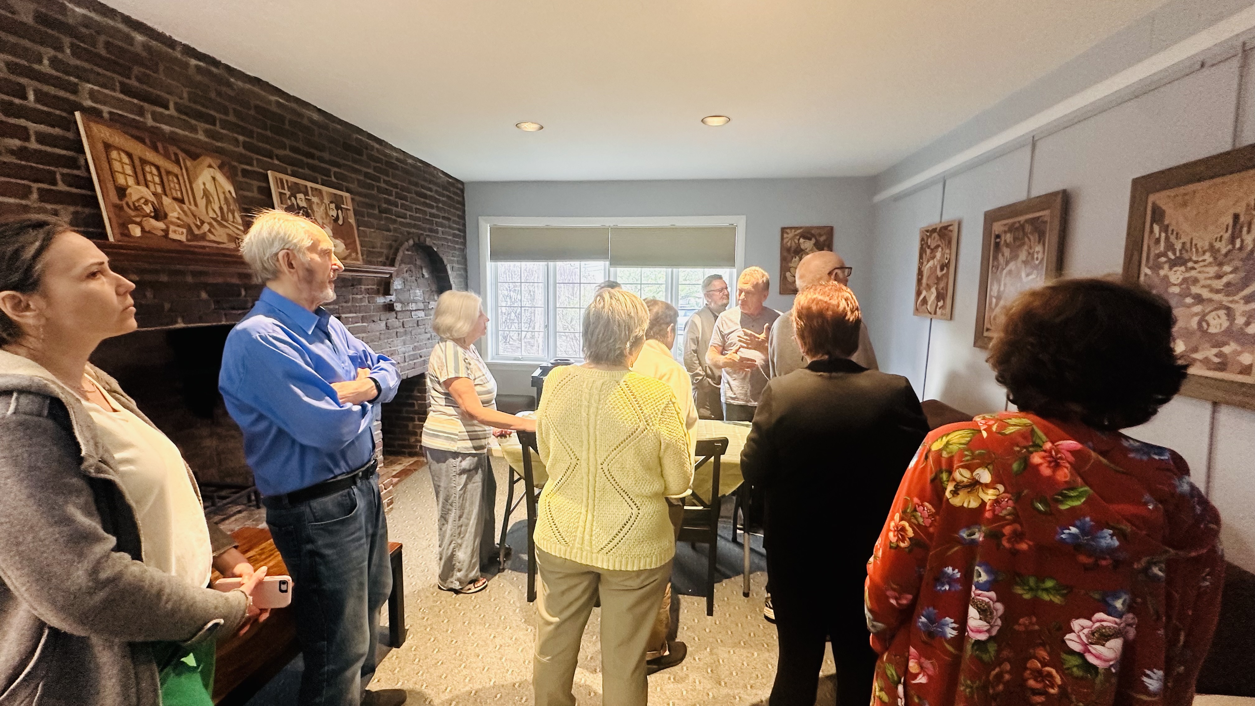 Visitors gathered in a room discussing marquetry works displayed on the wall